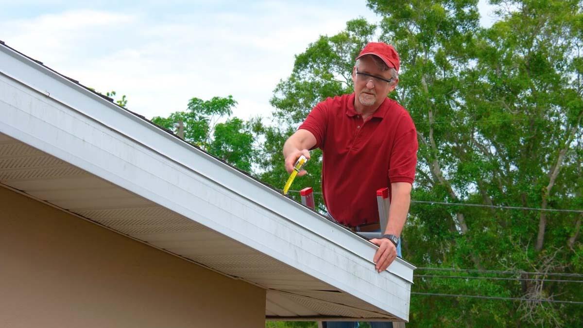 A man in a red shirt inspects the roof of a house