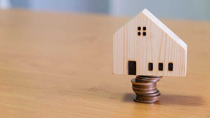 Wooden house on top of coins to represent refinancing a home